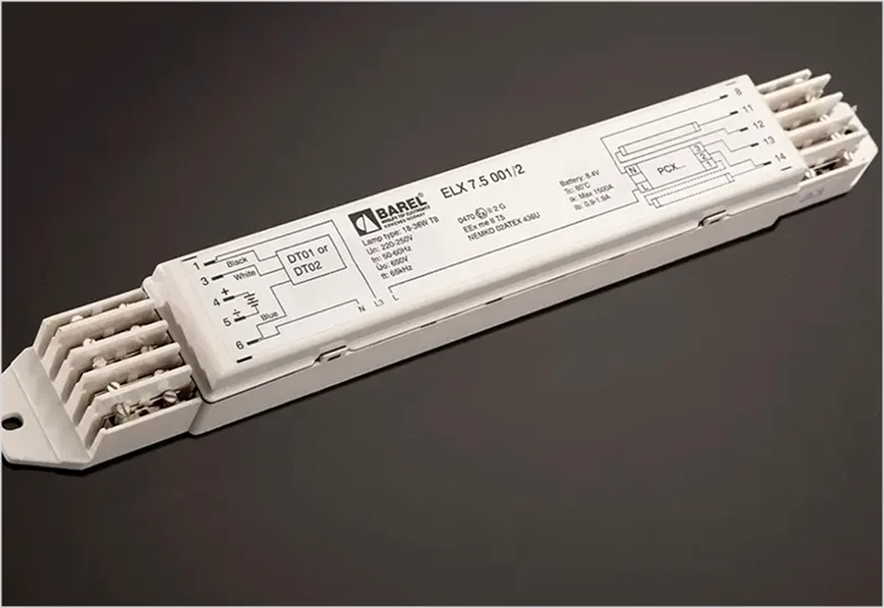 White electronic ballast with printed specifications and wiring diagrams, featuring terminal blocks on its ends against a dark background.