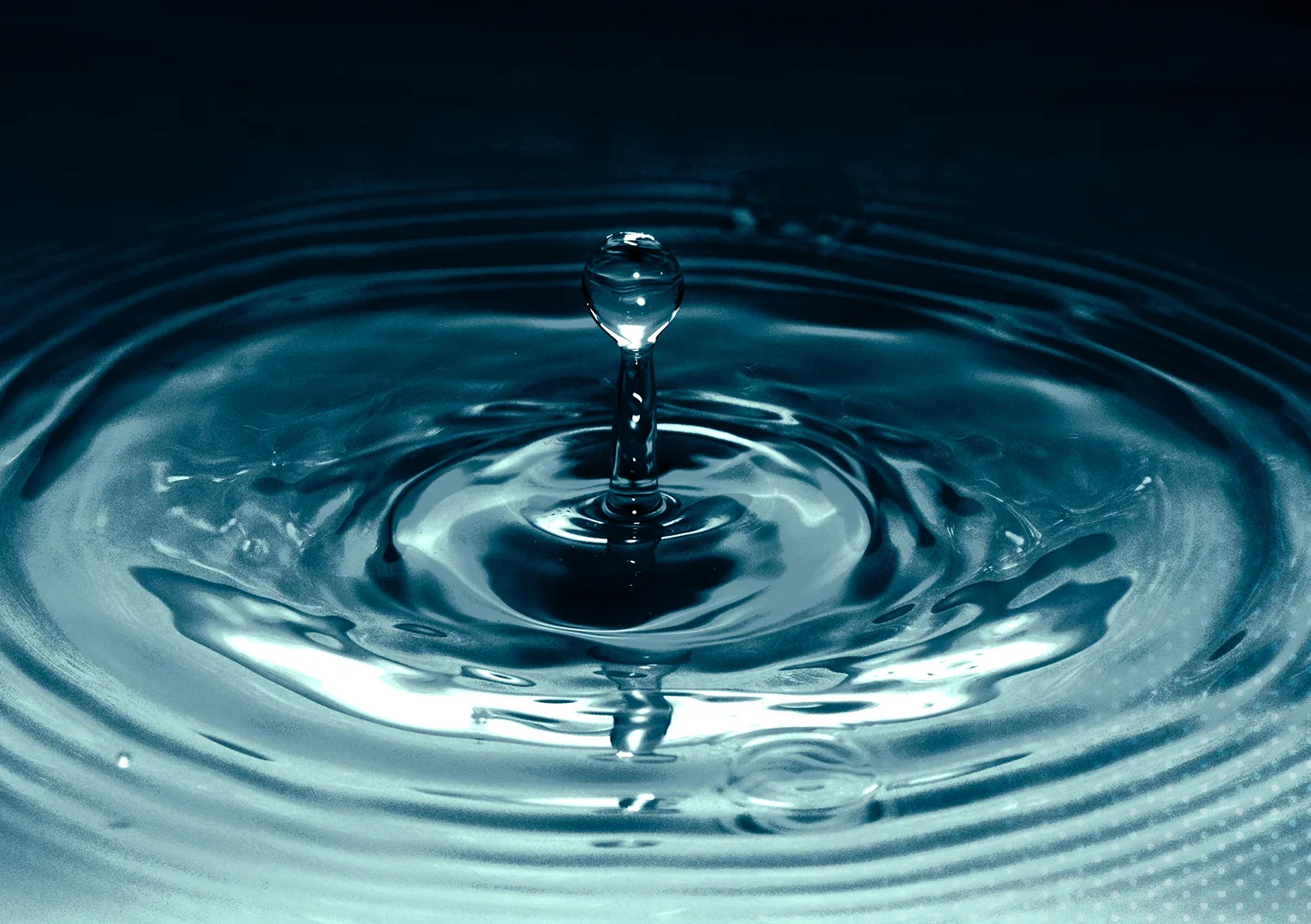 A clear water drop splashes into still water, creating concentric ripples across the surface.