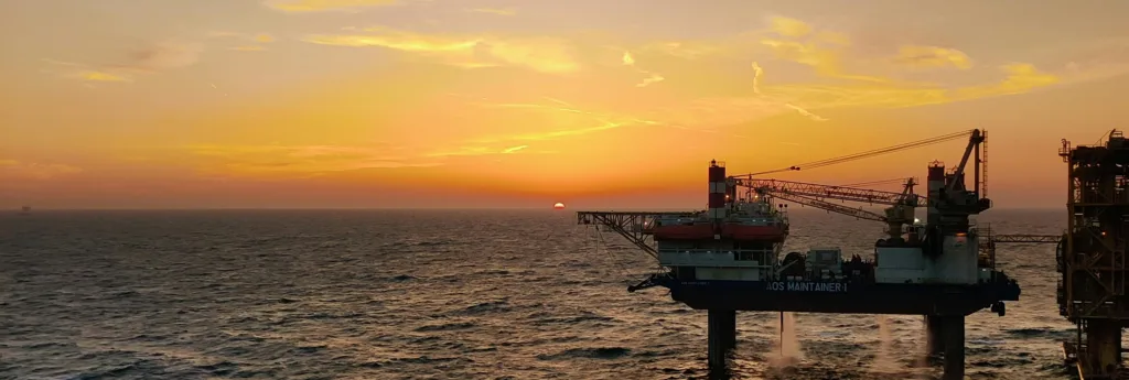 Offshore oil rig at sunset, with a vibrant orange sky over the calm sea.