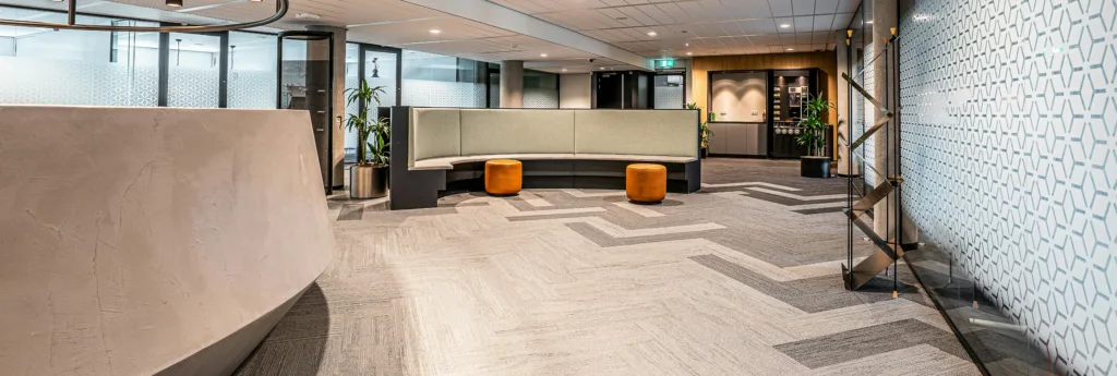 Modern office lobby with a curved reception desk, upholstered seating, and geometric carpet pattern.