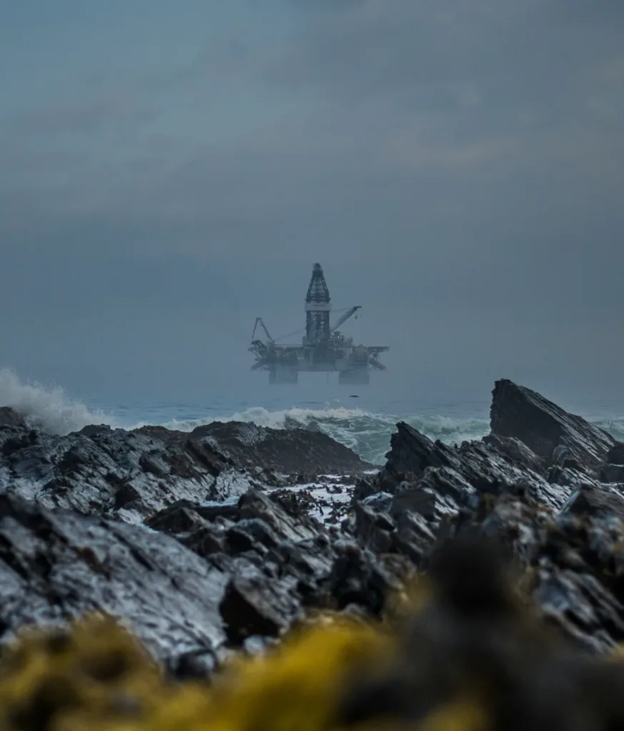Offshore oil rig in a stormy sea, viewed from a rocky shore with a seagull.