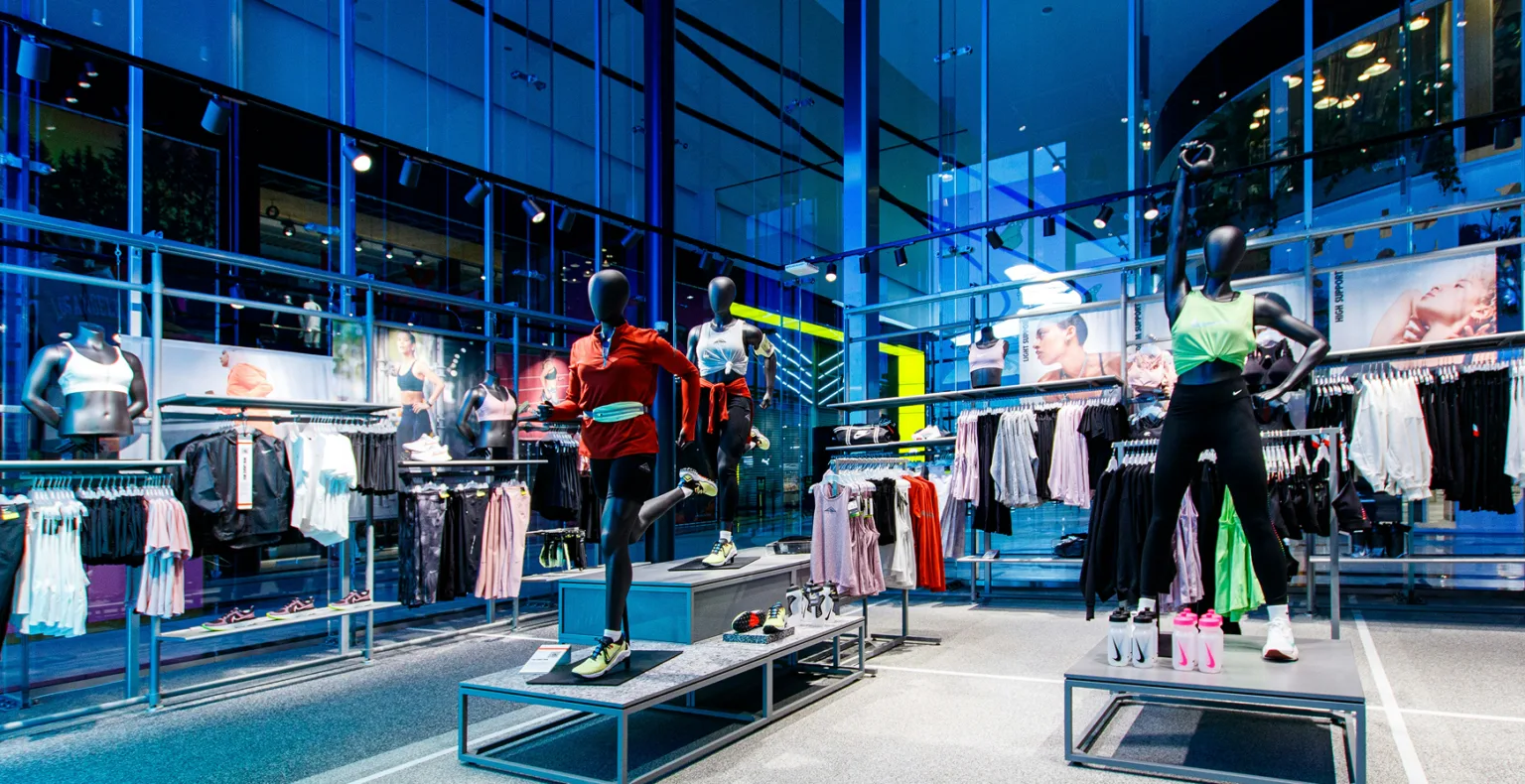 Interior of a modern retail store with sportswear on mannequins and racks, illuminated by blue lights.