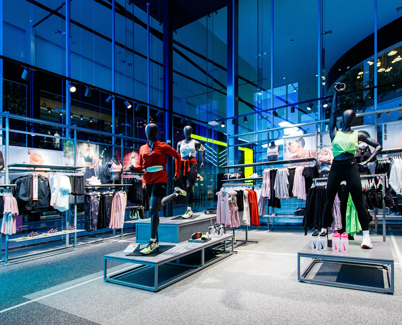 A modern athletic wear store interior with mannequins displaying sportswear, surrounded by clothing racks under blue lighting.