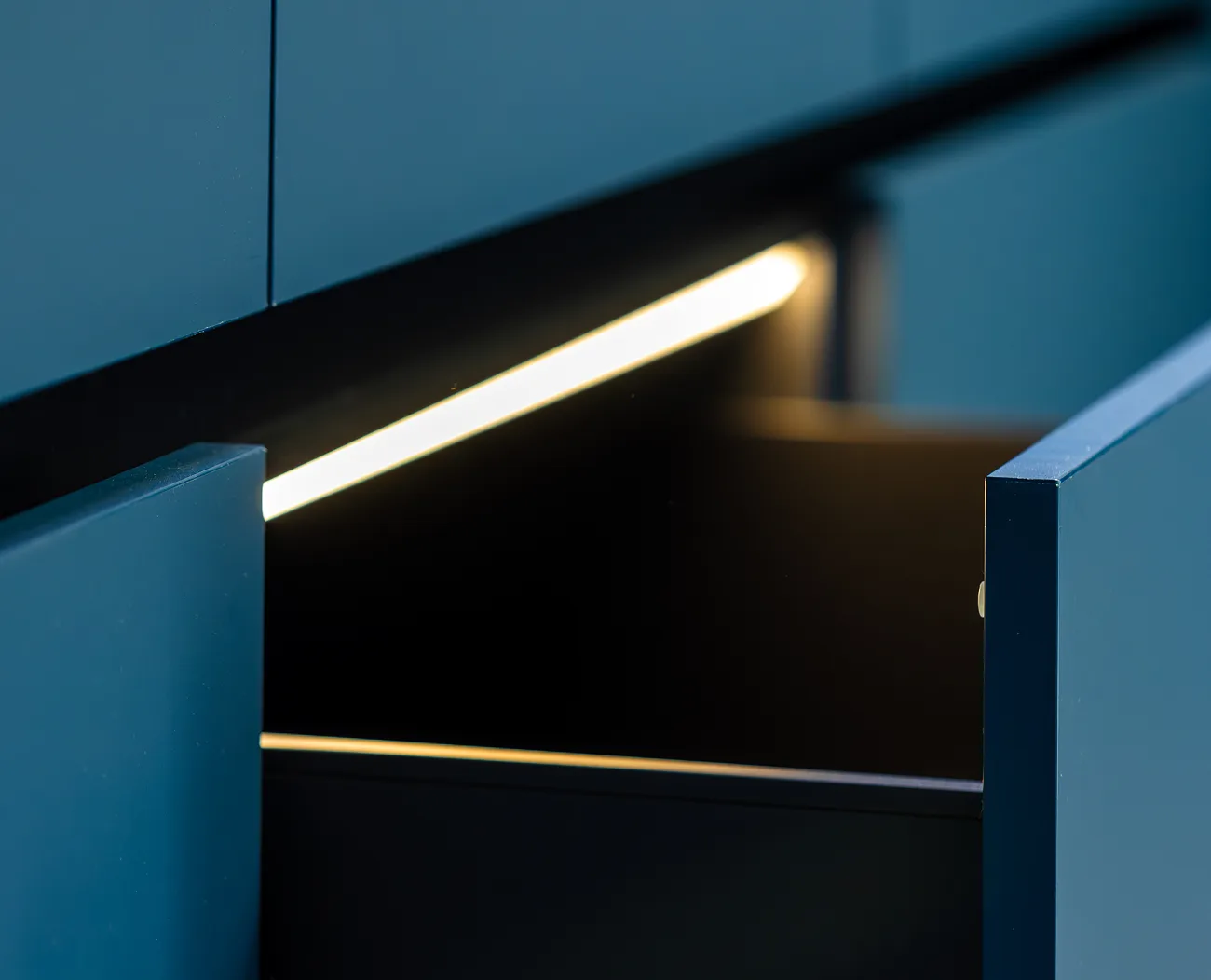 Partially opened dark blue drawers with internal warm LED strip lighting.