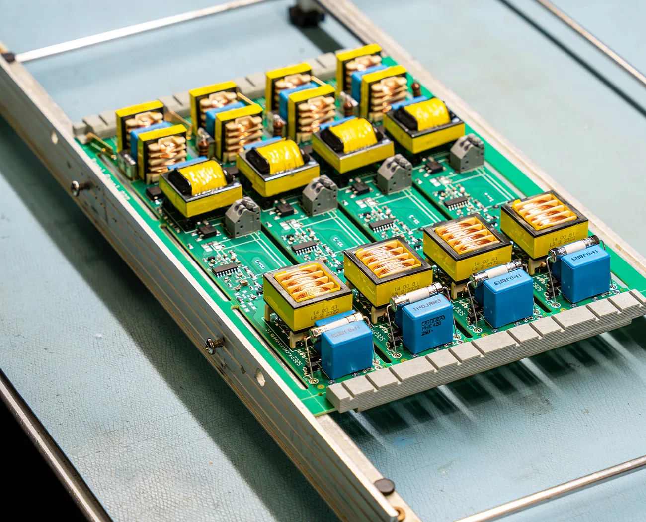 Electronic circuit boards featuring rows of yellow transformers and blue capacitors, neatly arranged in a specialized rack.