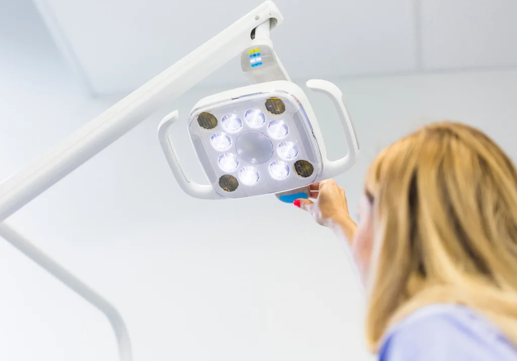 A person adjusts a bright, white dental lamp with LED lights.