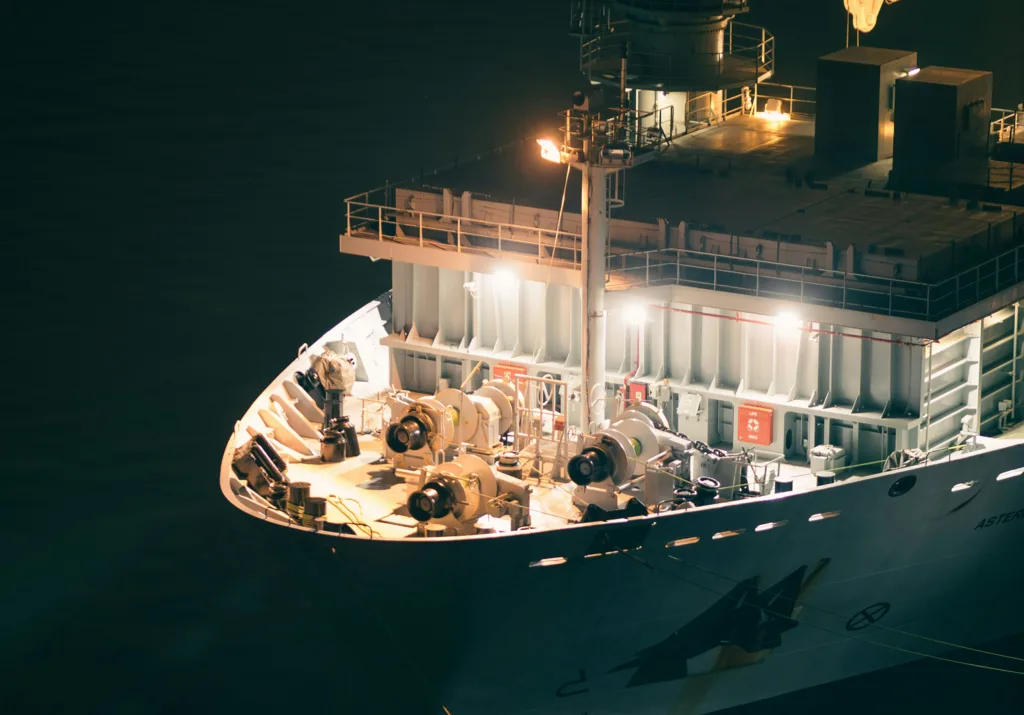 Close-up of the brightly lit bow of a large ship at night, showcasing deck machinery and equipment.