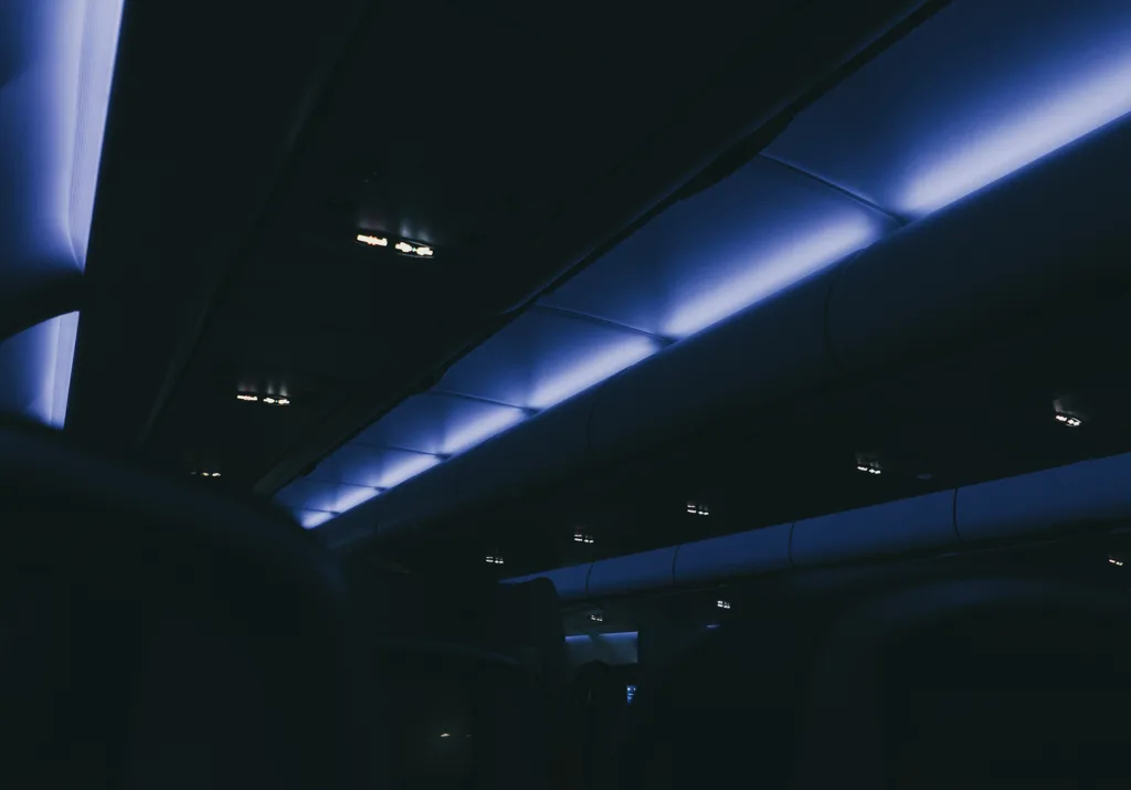 Interior of an airplane cabin with blue ambient lighting and overhead storage compartments visible.