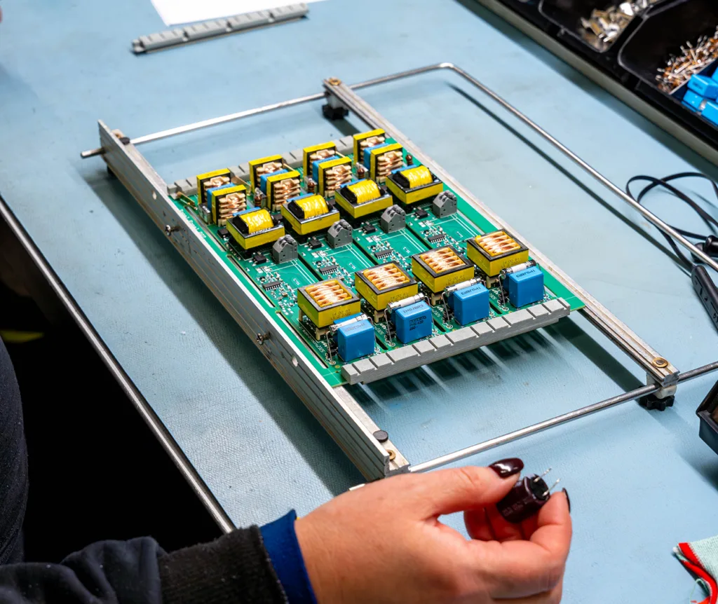 A green circuit board filled with yellow transformers and blue capacitors in a metal assembly frame.