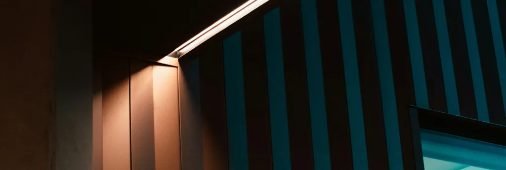 A brightly lit corner with vertical black and blue striped walls and a textured, dotted dark wall.