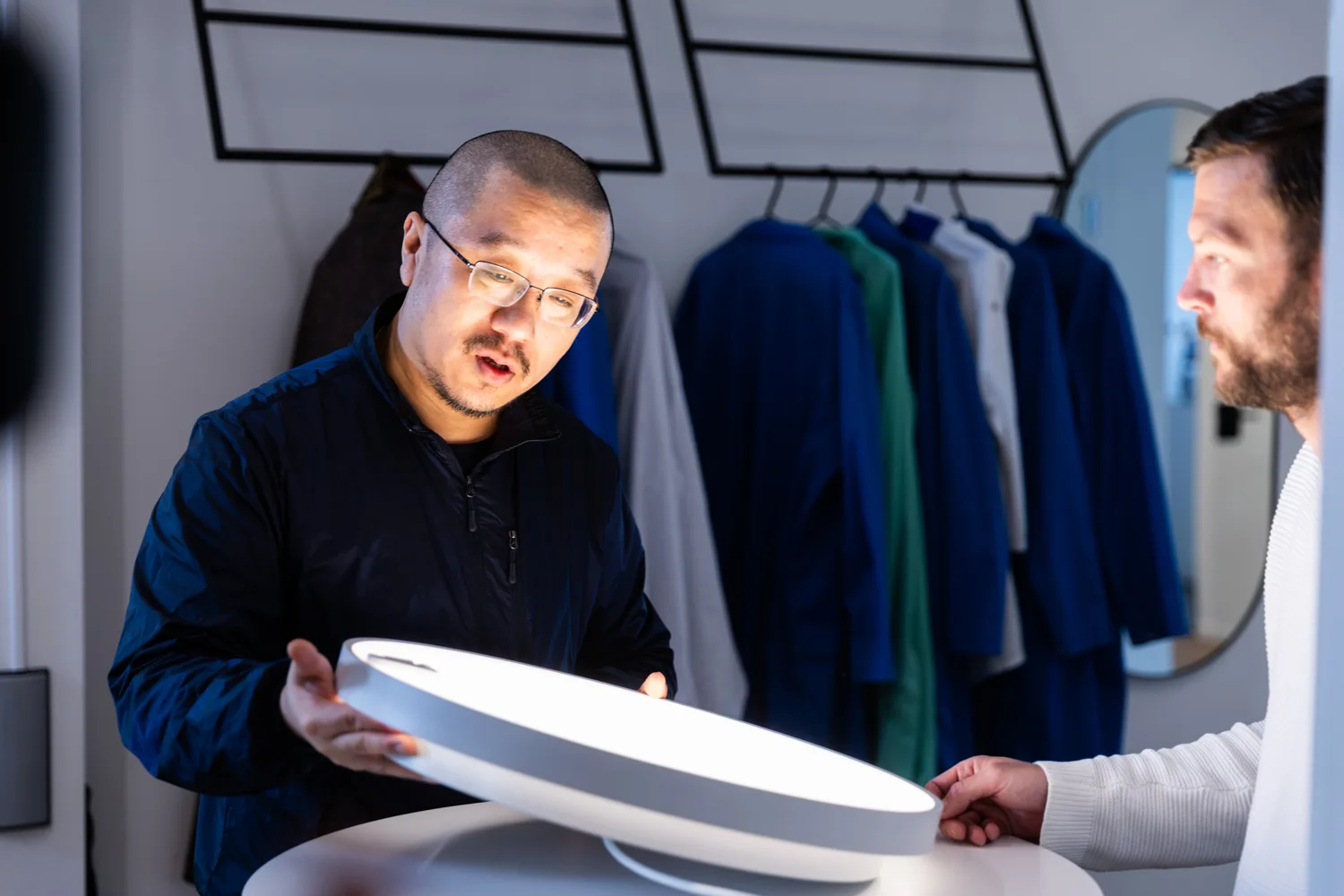 Two men examining a round, glowing device on a table, with one man holding it and the other looking on.