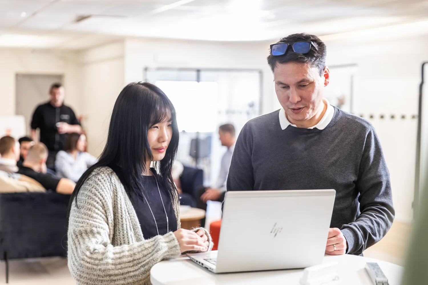 Two colleagues, a woman and a man, collaborating on a silver laptop at a standing desk.