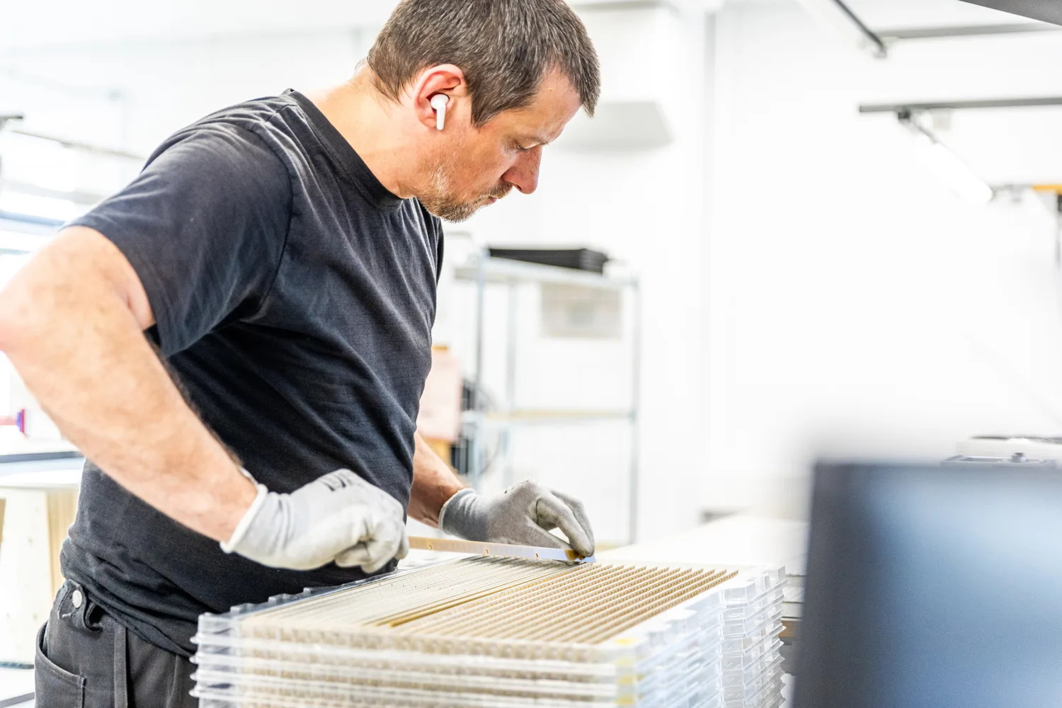 A focused worker in a black shirt and gloves assembling components on a production line.