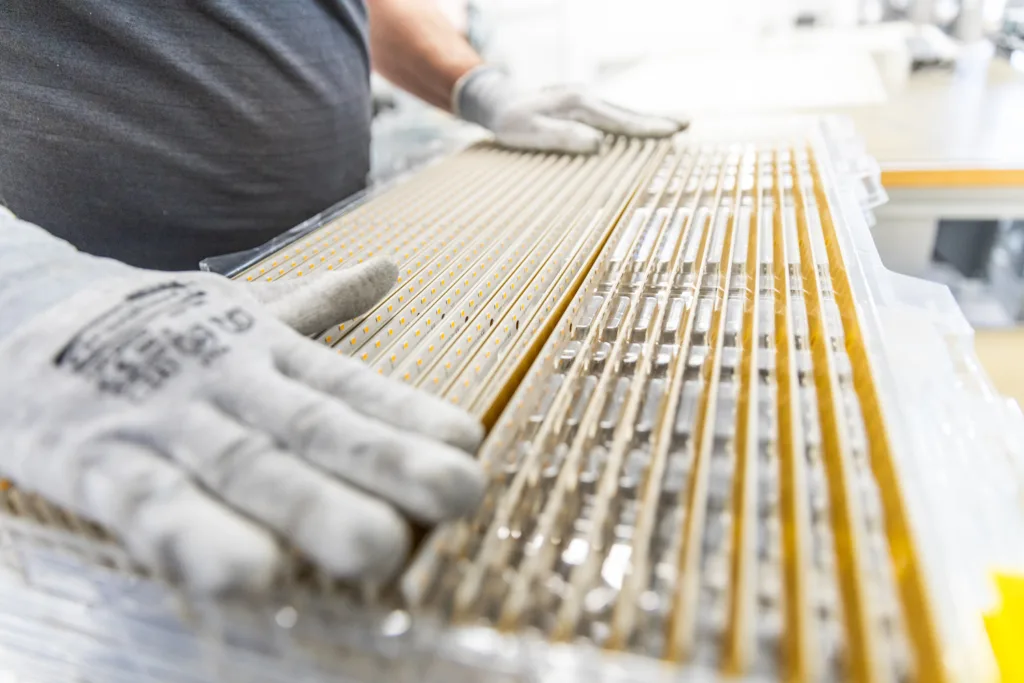 Close-up of gloved hands assembling or inspecting multiple LED light strips in a factory setting.