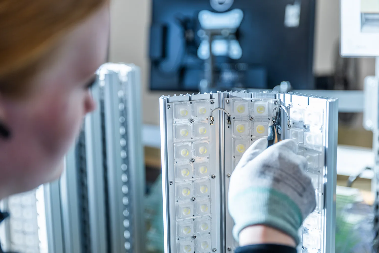Close-up of an LED light fixture being assembled, showing rows of bright white LED components and a gloved hand.