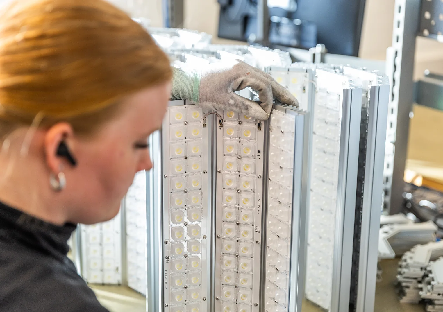 Close-up of a gloved hand assembling LED lighting modules in a factory. The modules contain multiple individual LED lights.